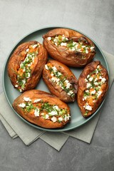 Tasty cooked sweet potatoes with feta cheese, green onion and parsley on gray textured table, top view