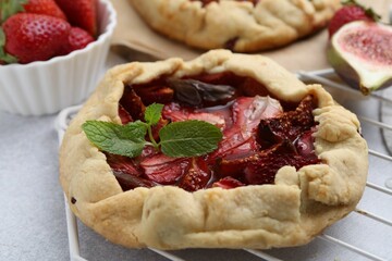 Tasty galette with strawberries, figs and mint on light table, closeup