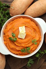Tasty mashed sweet potato with butter in bowl, fresh vegetables and parsley on table, flat lay