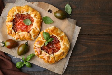 Tasty galettes with tomato and basil on wooden table, flat lay. Space for text