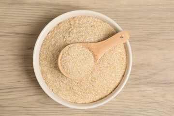 Oat bran in bowl and spoon on wooden table, top view