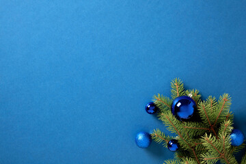 Festive Christmas corner with vibrant blue ornaments on a lush fir branch against a bold blue...