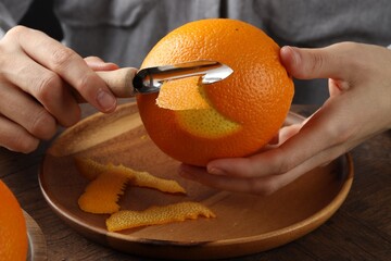 Woman zesting orange at wooden table, closeup