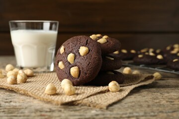 Tasty chocolate cookies with hazelnuts and milk on wooden table, closeup