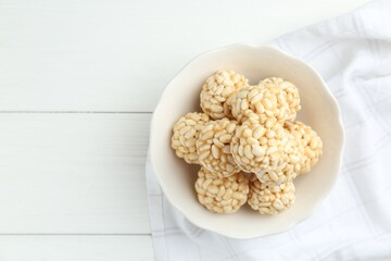 Tasty puffed rice balls in bowl on white wooden table, top view. Space for text