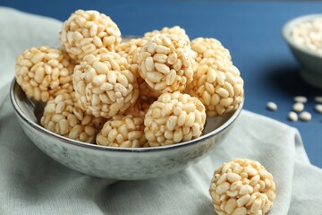 Tasty puffed rice balls in bowl on blue table, closeup