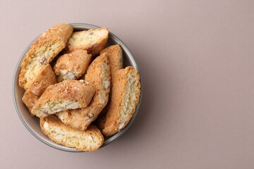 Tasty almond biscuits (Cantuccini) in bowl on beige background, top view. Space for text