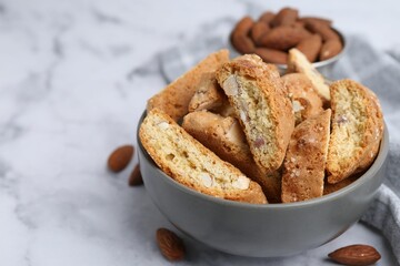 Tasty almond biscuits (Cantuccini) in bowl and nuts on light marble table, closeup. Space for text