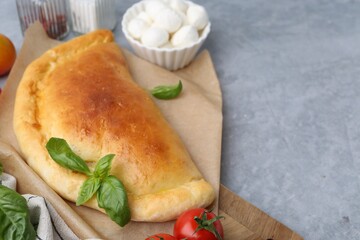 Tasty vegetarian calzone with basil, mozzarella cheese and tomato on grey table, closeup. Space for text
