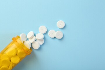 Bottle of antibiotic pills on light blue background, top view. Space for text