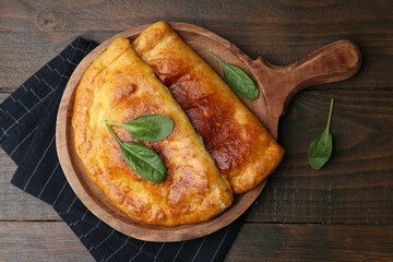 Tasty calzones with basil on wooden table, top view