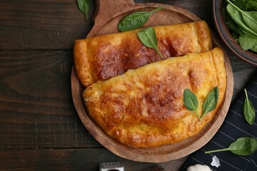 Tasty calzones with basil on wooden table, top view