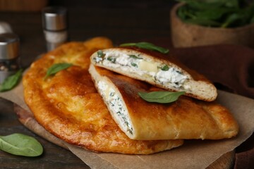 Tasty calzones with cheese and basil on wooden table, closeup