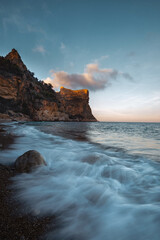 The rock rises above the blue sea at sunset or sunrise