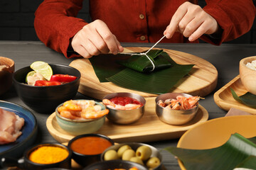 Woman tying banana leaf with food at wooden table with products, closeup. Healthy eco serving