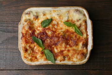 Delicious cooked lasagna in baking dish and basil on wooden table, top view
