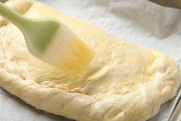 Brushing egg yolk onto uncooked calzone pizza, closeup