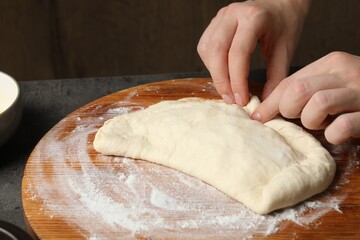 Woman making calzone pizza at grey table, closeup