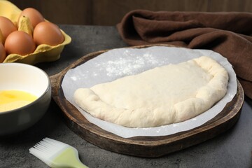 Uncooked calzone pizza and eggs on grey table