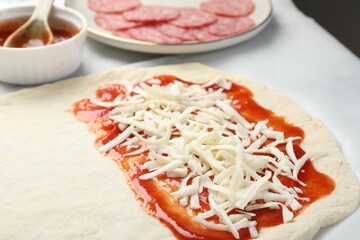 Making calzone pizza. Dough with sauce, cheese and other ingredients on table, closeup