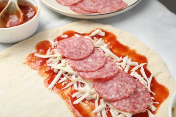 Making calzone pizza. Dough with sauce and stuffing on table, closeup