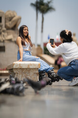 Young woman taking photo of friend wearing inline skates in city park