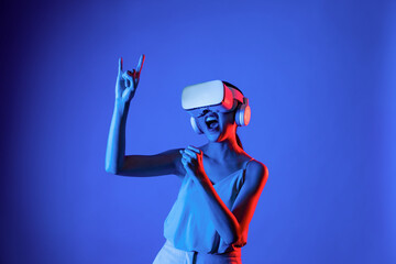 Smart female standing surrounded by neon light wearing VR headset connecting metaverse, future cyberspace community technology. Elegant woman enjoy dancing wavering body and sing song. Hallucination.