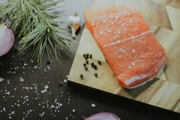 Fresh red salmon on wooden tray with coarse pepper, salt, garlic, red onion, red pepper and rosemary
