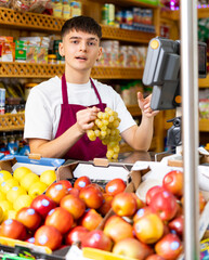 Male shopping assistant weighing grapes in grocery shop