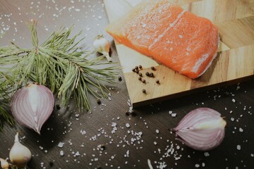 Fresh red salmon on wooden tray with coarse pepper, salt, garlic, red onion, red pepper and rosemary