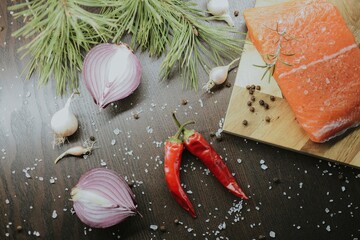 Fresh red salmon on wooden tray with coarse pepper, salt, garlic, red onion, red pepper and rosemary