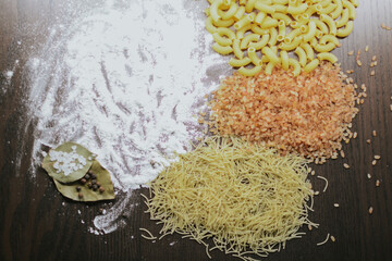 Types of pasta and pink rice with flour, bay leaf with coarse salt and pepper on a brown background