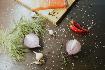 Fresh red salmon on wooden tray with coarse pepper, salt, garlic, red onion, red pepper and rosemary