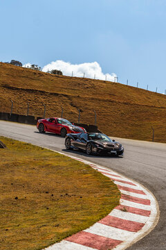 Black Ferrari F8 Spider turning on track kerb, Convertible supercar racing with red coupe behind