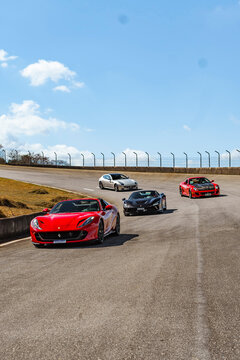 Red Ferrari 812 GTS and Black F8 Spider front view rolling shot on race track, Luxury supercars in track day event