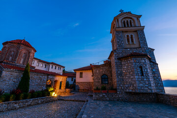 The monastery of Saint Naum, a historical landmark, glows warmly under the twilight sky, its stone...