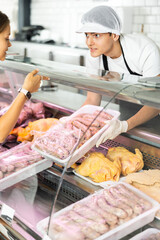 Knowledgeable male butcher proudly showcases finest cuts on his stand, guiding customer's choice.