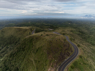  Aerial view of a curvy mountain black top road with beautiful landscape around it.