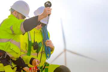 Two engineers wearing high visibility safety jackets and helmets measure wind speed with an...