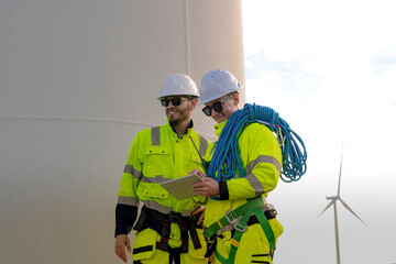 Two engineers in high visibility gear stand near a wind turbine, reviewing a clipboard and preparing for maintenance work. The image highlights teamwork, safety, and renewable energy sector.