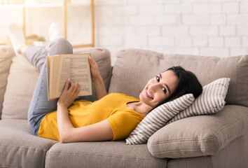 Lockdown leisure activities. Lovely young girl reading book while lying on sofa at home