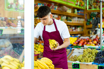 Focused male seller lay out ripe banana on counter in supermarket