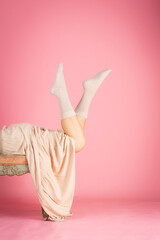 Model wearing socks lying on chaise longue raising legs on pink background