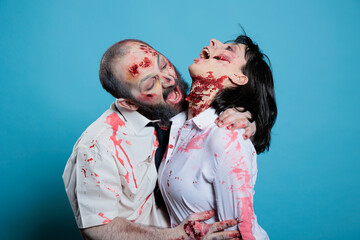 Actor biting costar on neck on studio background horror movie set dressed as undead zombies. Man...