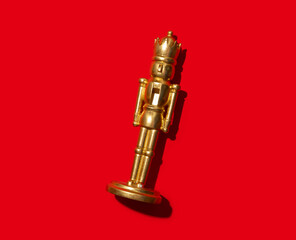 A golden nutcracker figurine standing upright against a bold red background. This minimalist and...