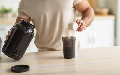 Cropped view of young fit guy making protein shake in kitchen, closeup. Unrecognizable millennial...