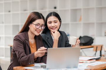 Two businesswomen working together on a laptop in a contemporary office, discussing ideas and enjoying coffee.