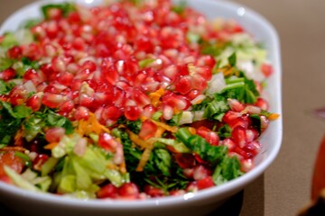 Vitamin-packed winter Christmas salad decorated with pomegranate seeds. Christmas salad with pomegranate, carrots and dill on a white plate, close-up. New Year's table special salad.
