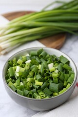 Chopped green onion in bowl on white table, closeup
