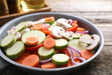 Frying pan with mix of fresh vegetables and mushrooms on wooden table, closeup
